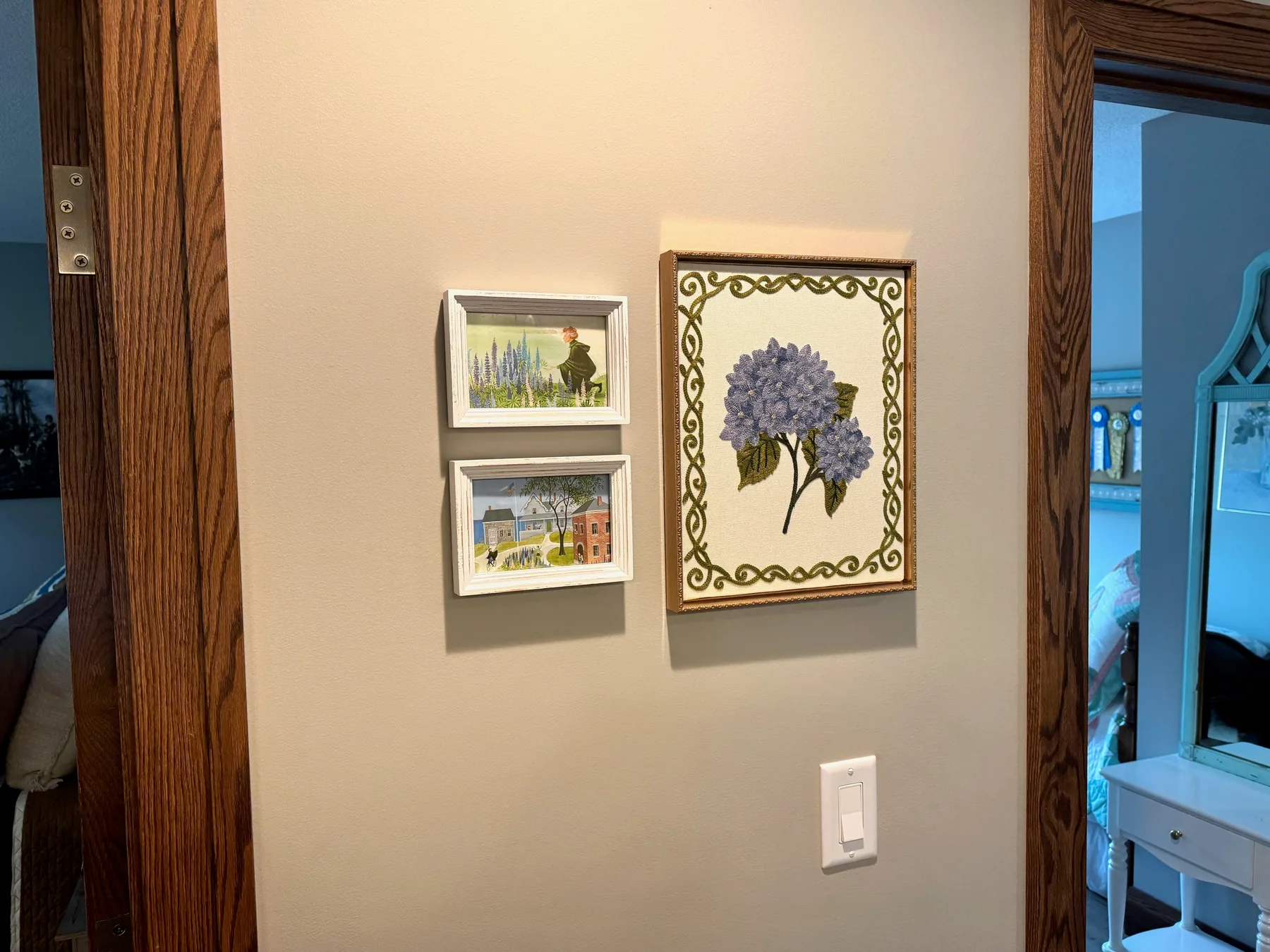 The framed Miss Rumphius scenes and floral needlework hanging between two upstairs rooms at Grey Cloud Island