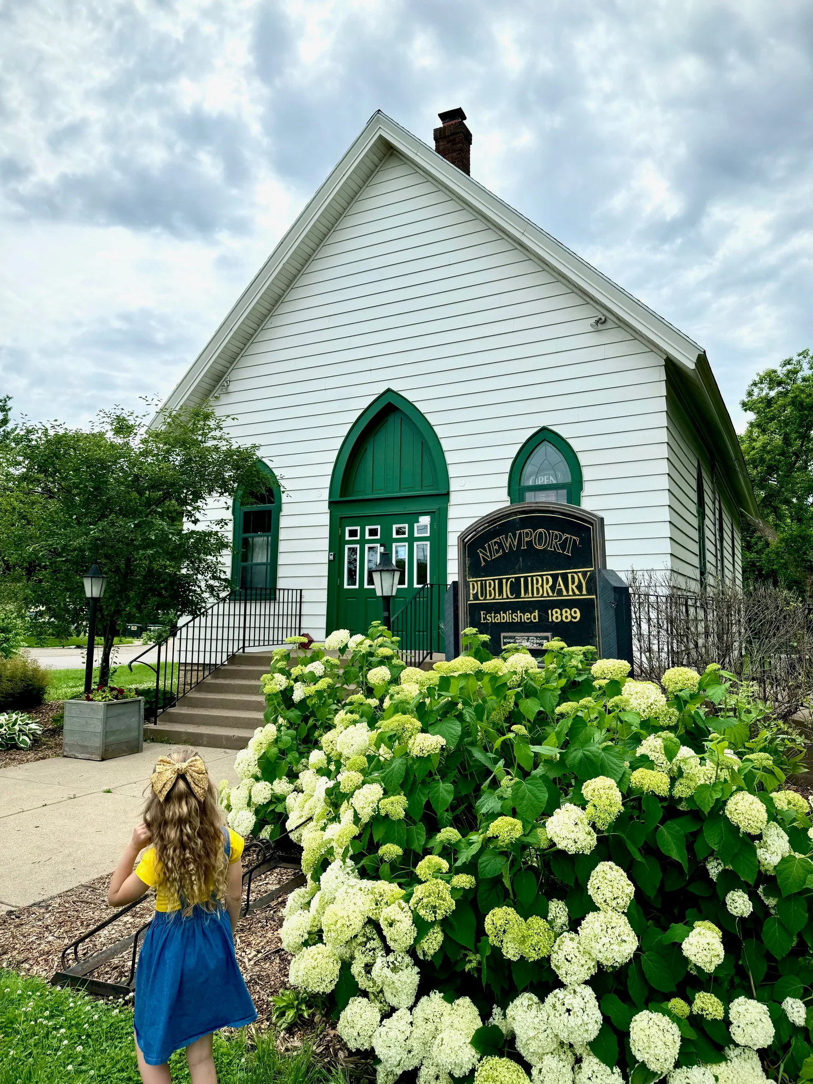 The white-and-green Newport Library in its historic church building, with hydrangeas blooming beside the front walk