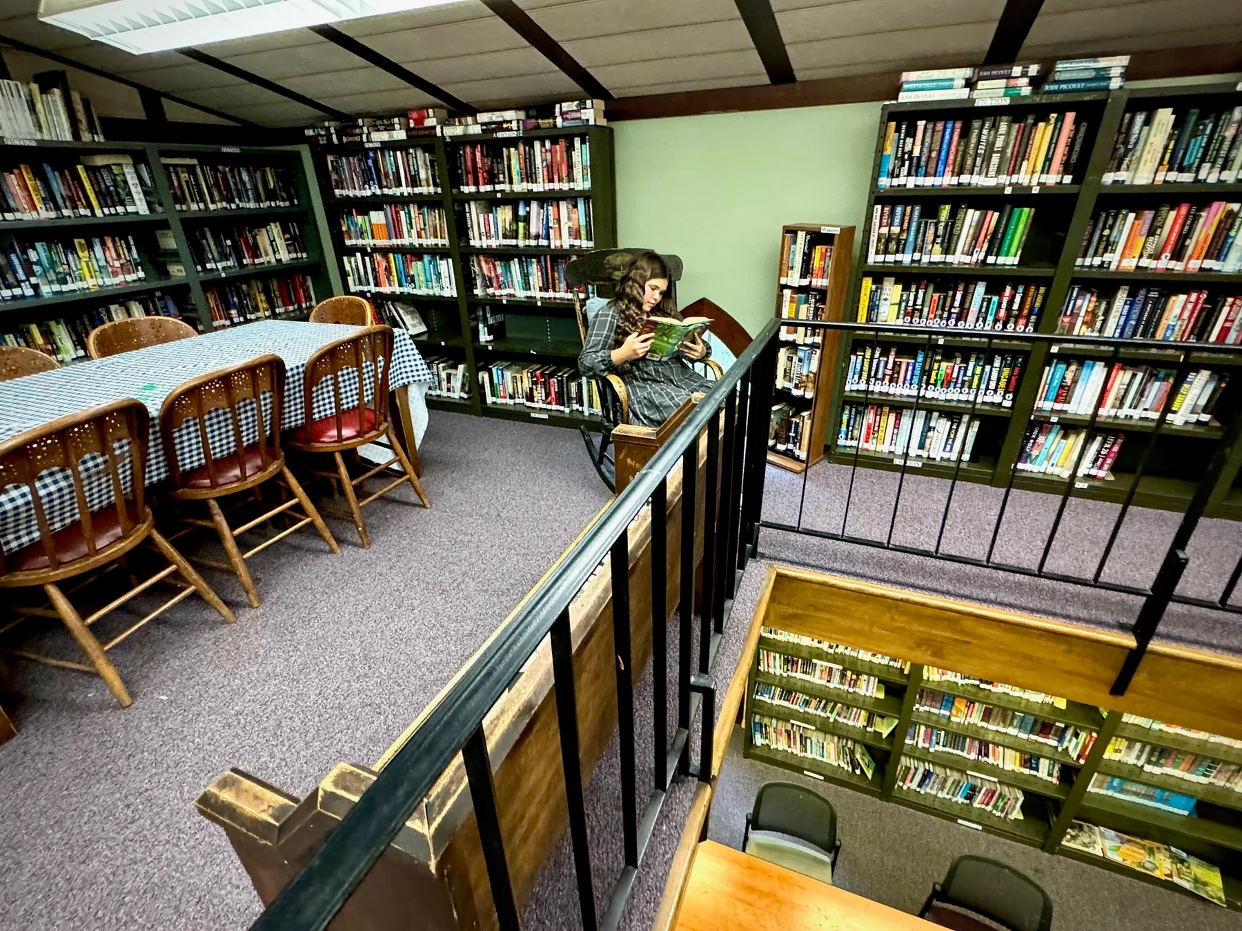 A young reader sitting in a rocking chair in the book-lined upper loft of the Newport Library
